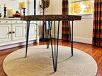 Round wooden table with metal legs in a room with a rug, cabinets, and curtains.