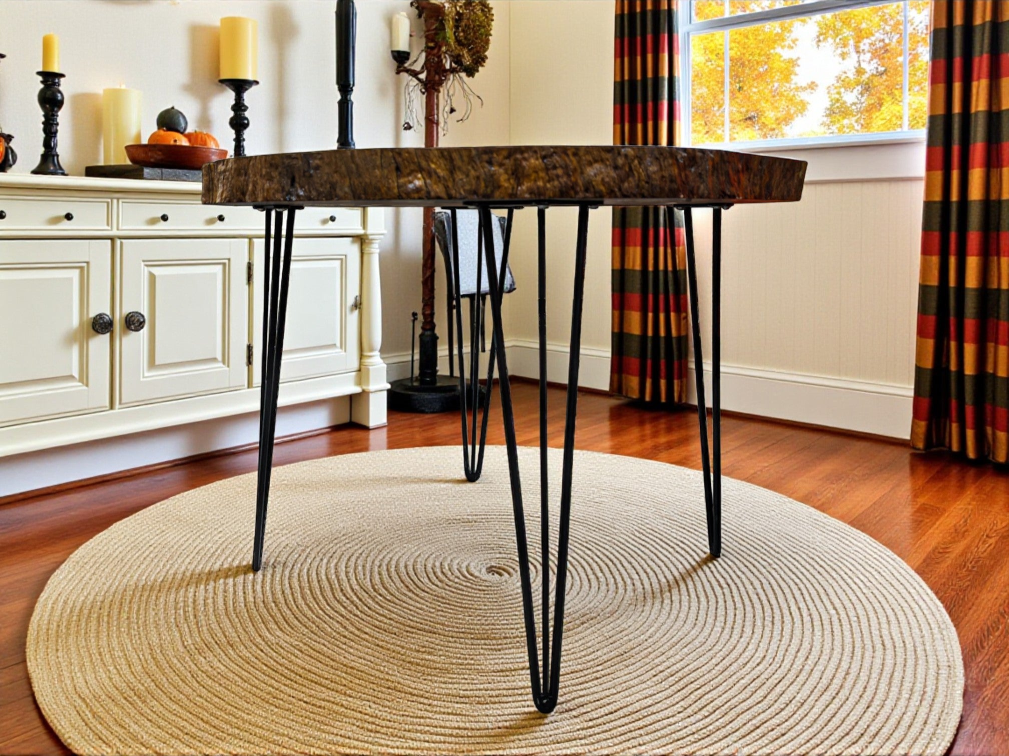 Round wooden table with metal legs in a room with a rug, cabinets, and curtains.