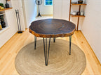 Wooden table with a natural edge design on a round jute rug in a room with wooden flooring.